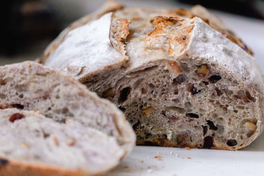 sourdough cranberry bread loaf with a slice cut off on a white countertop