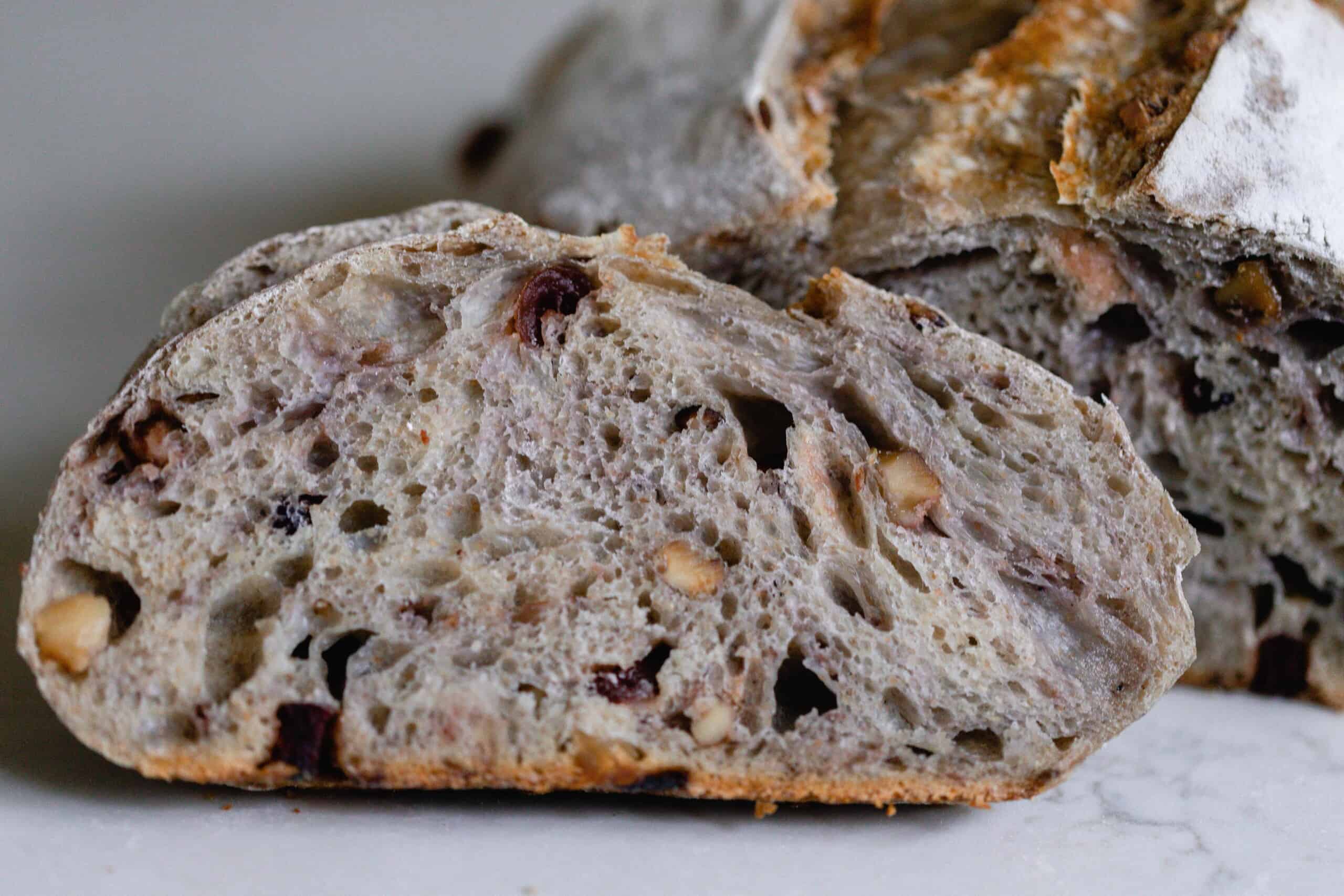 a slice of sourdough cranberry walnut bread propped up on the rest of the loaf on of a white countertop