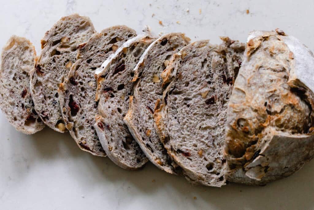 a cranberry sourdough bread boule sliced up on a white countertop