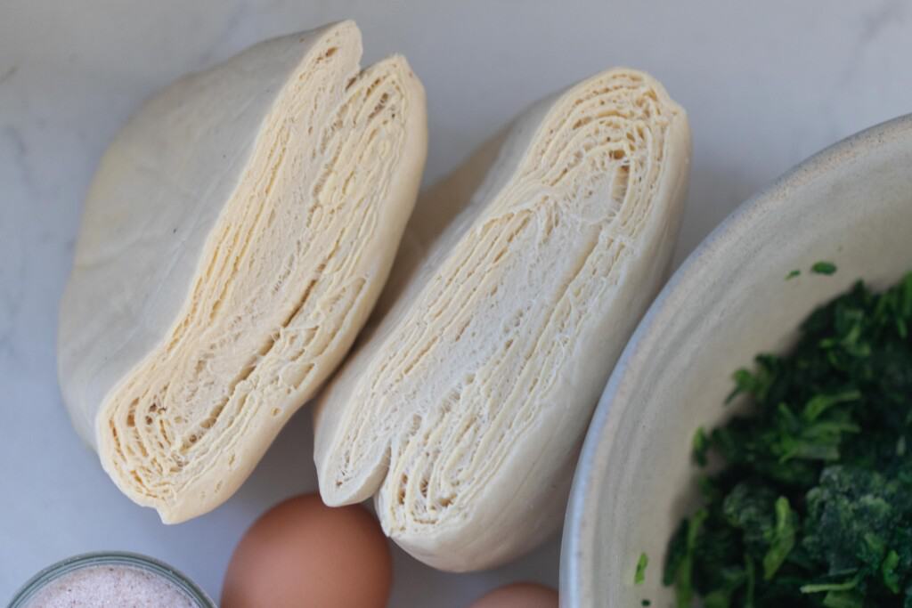 puff pastry on a white counter next to a bowl of frozen spinach and two eggs