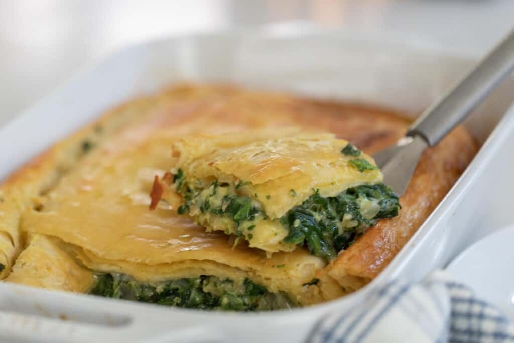 a spatula with a slice of spinach pie resting on top of the remaining pie in a white baking dish