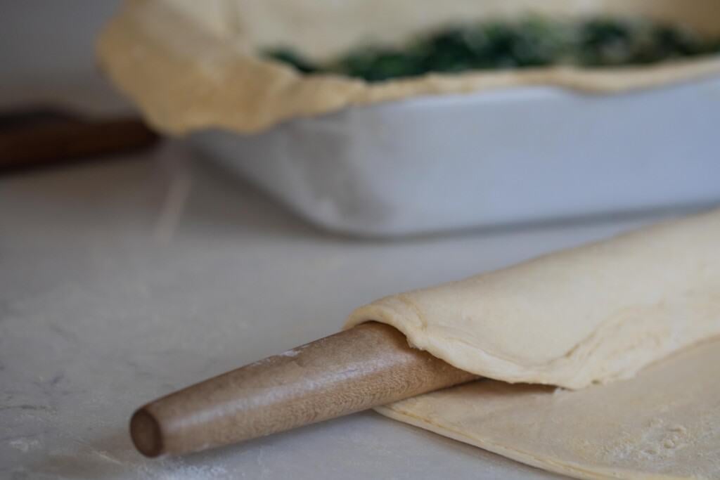 rolling out the second puff pastry to add to the top of a spinach pie