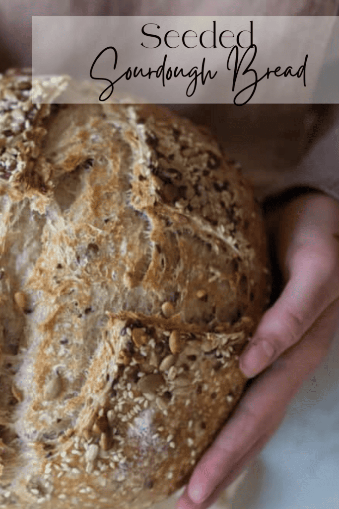 A hand holding a seeded sourdough loaf