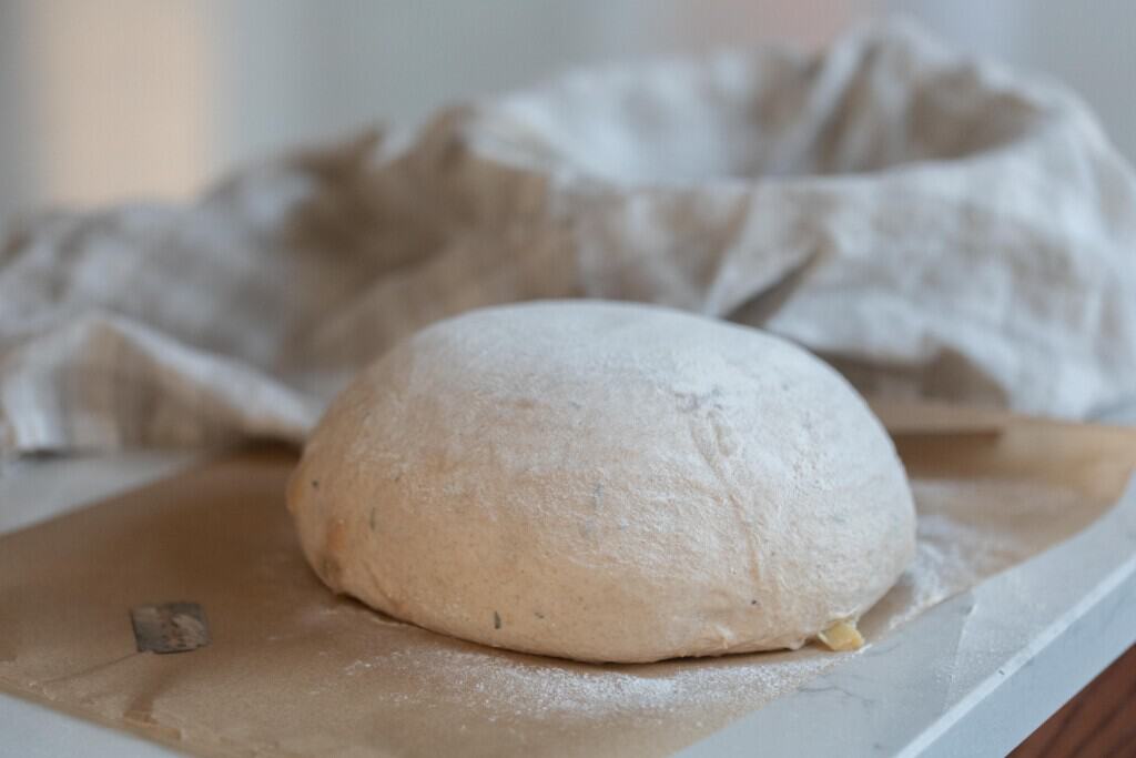 bread dough on a white countertop with a towel lined basket in the background 