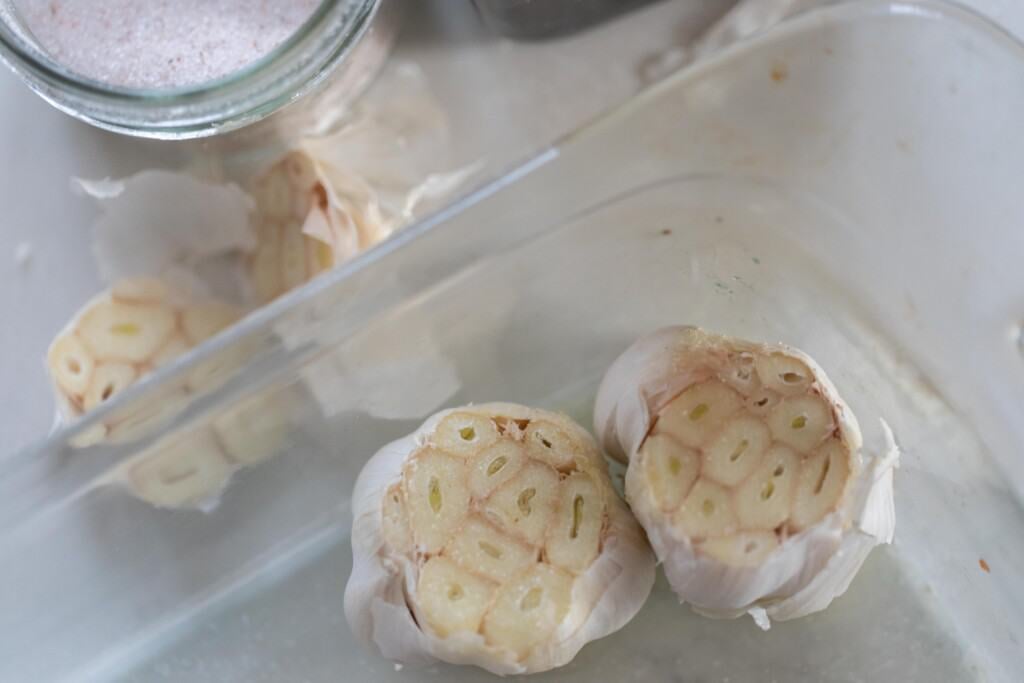 two heads of garlic with their tops cut off. The garlic is in a glass baking dish