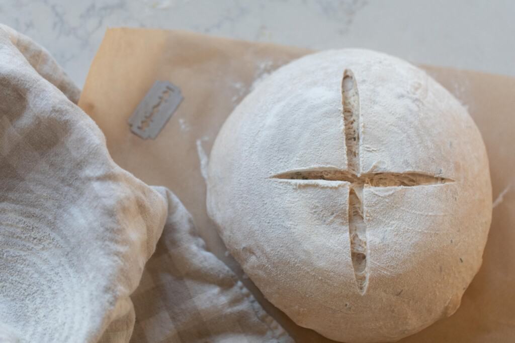 bread dough with a x slapped on the top. The dough sits on parchment paper