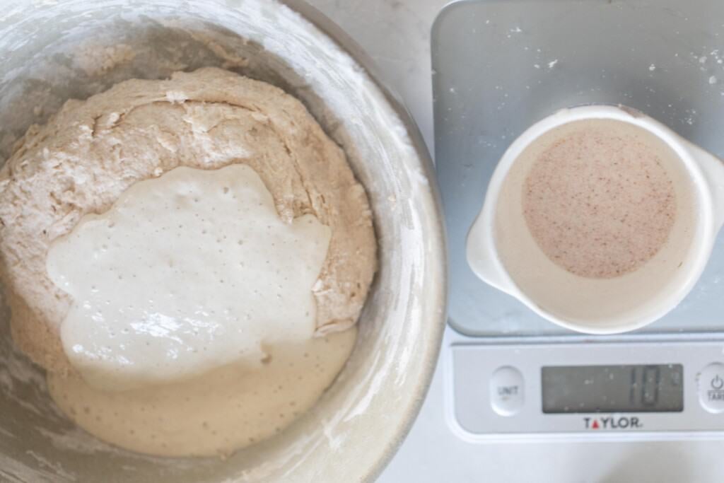 Large bowl with sourdough dough next to a kitchen scale with ingredients being measured on top