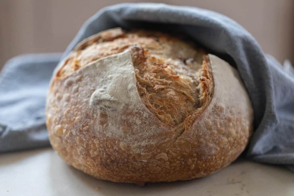 boule of garlic sourdough bread wrapped in a blue towel on a white countertop
