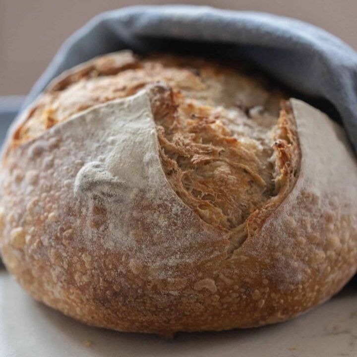 boule of garlic sourdough bread wrapped in a blue towel on a white countertop