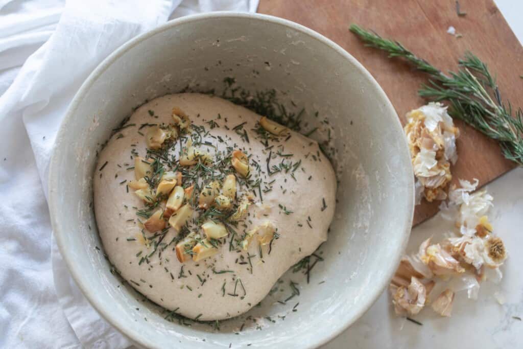 roasted garlic and rosemary added to the top of bread dough in as bowl