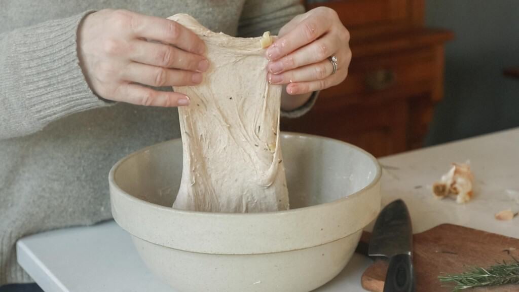 hands pulling up dough in a stoneware bowl 