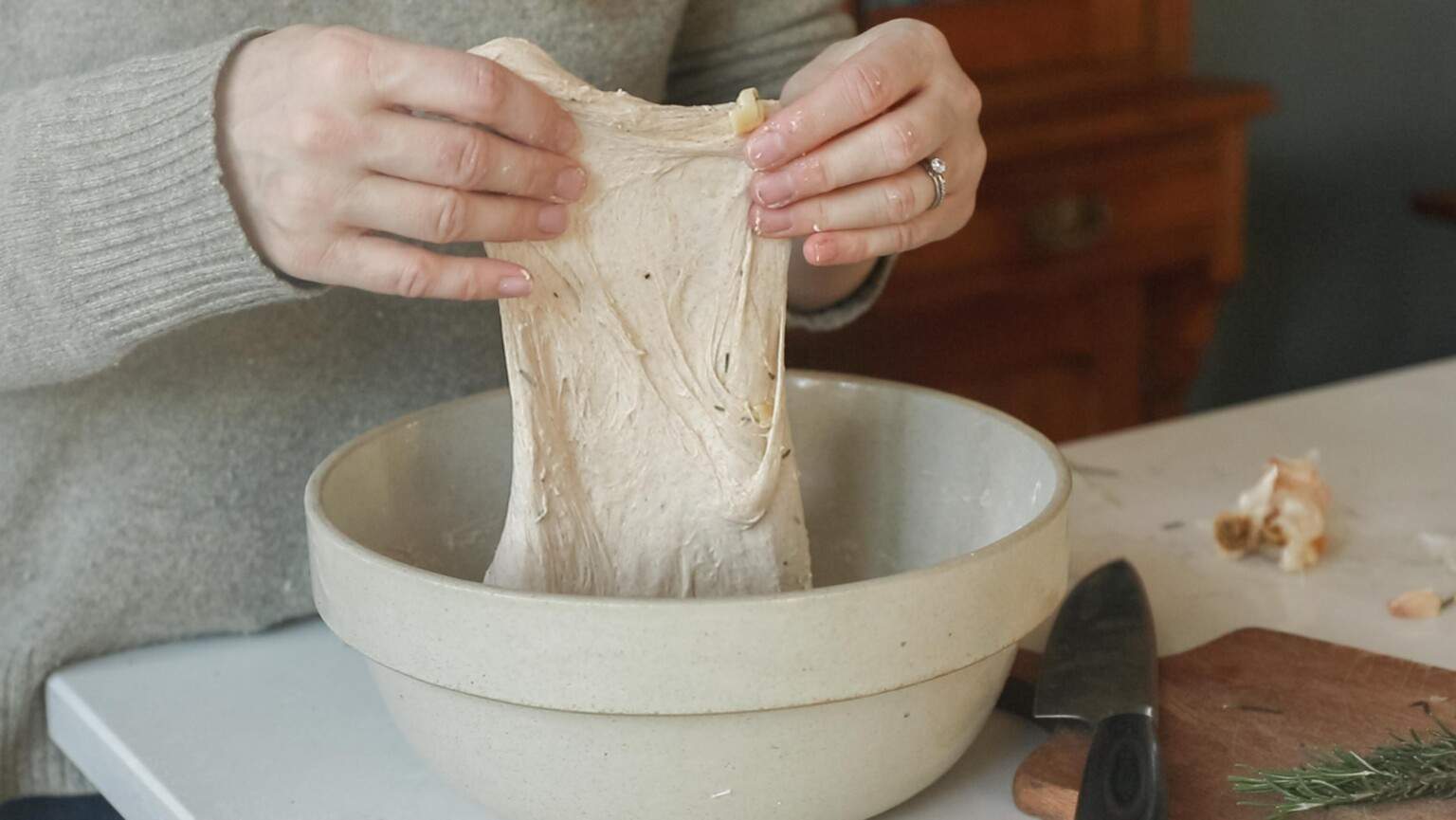 hands pulling up dough in a stoneware bowl