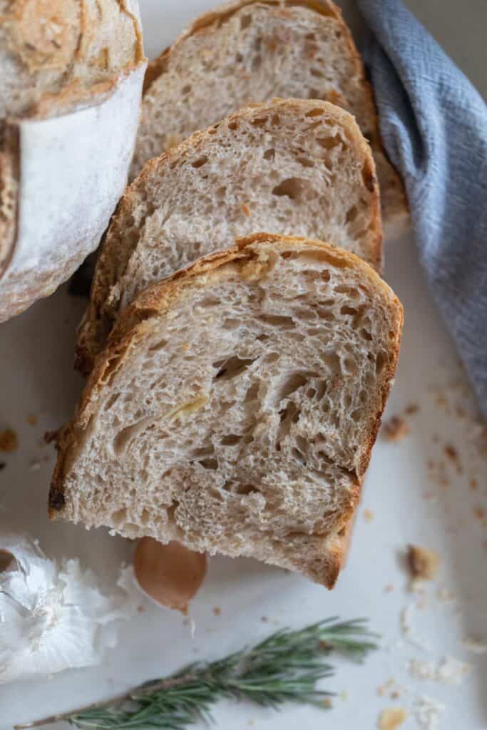 overhead photo of three slices of rosemary garlic sourdough bread on a white countertop