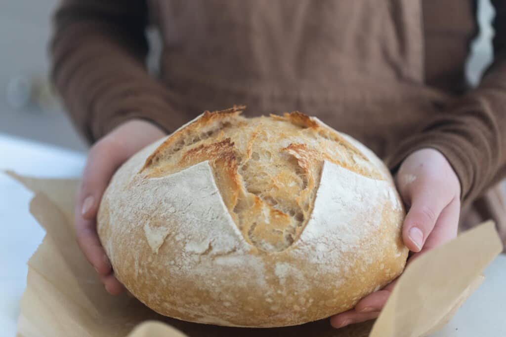 Woman holding a boule of high hydration sourdough with parchment paper underneath it.