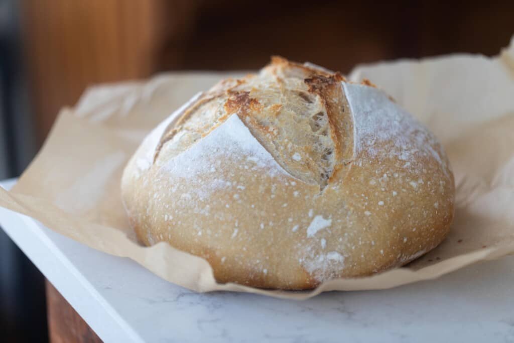 High hydration sourdough loaf fully baked on a parchment paper on white countertop