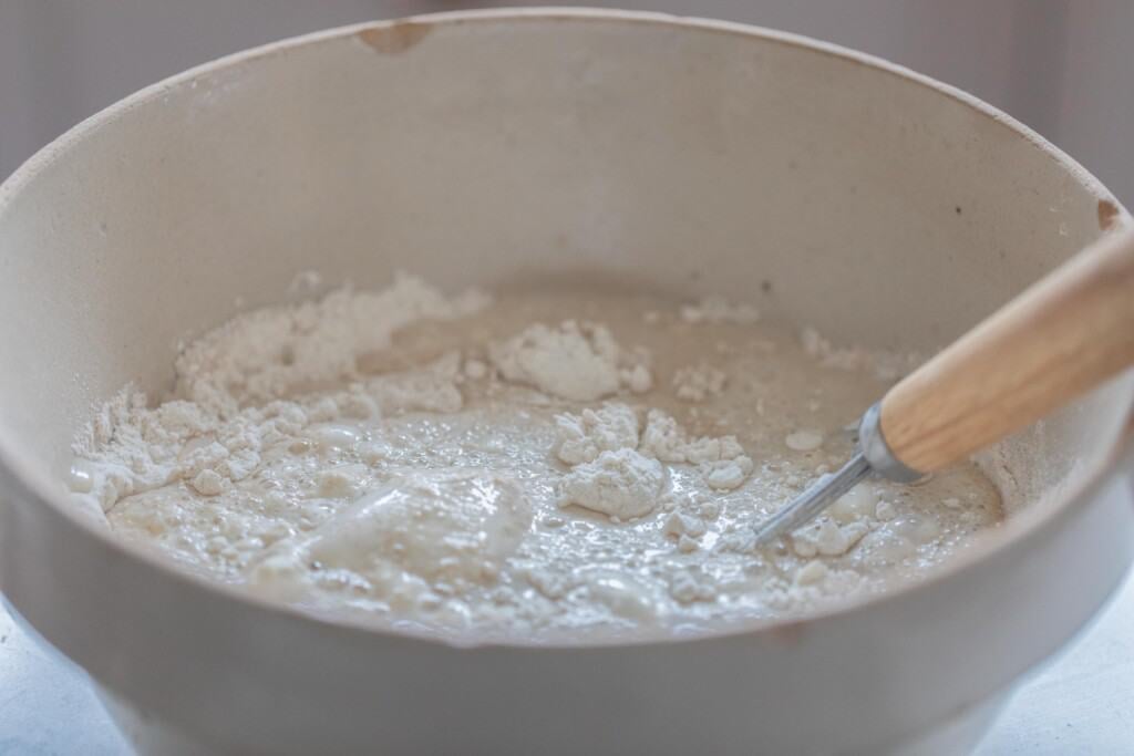 honey sourdough bread ingredients in a white bowl with a dough whisk