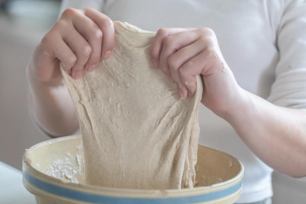 two hands sretching dough for honey sourdough bread in a white bowl