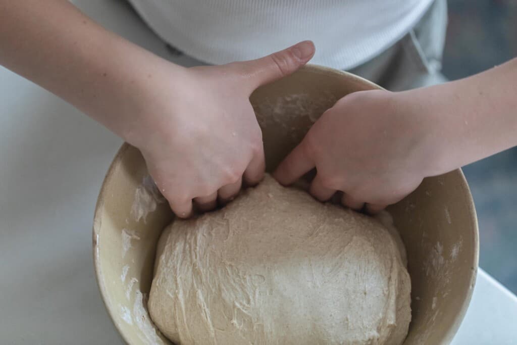 two hands folding dough back into tan bowl