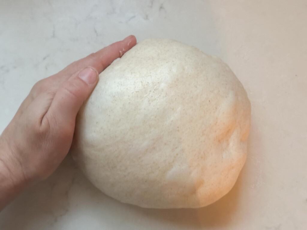 a hand shaping a honey sourdough bread dough ball on a white countertop