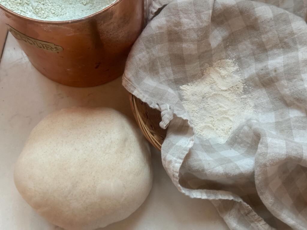 honey sourdough bread dough in a ball next to a bowl with a tea towel filled with flour