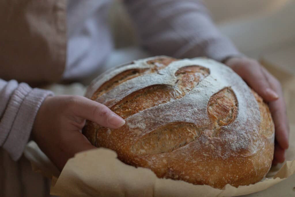 two hands picking up a golden brown loaf of honey sourdough bread