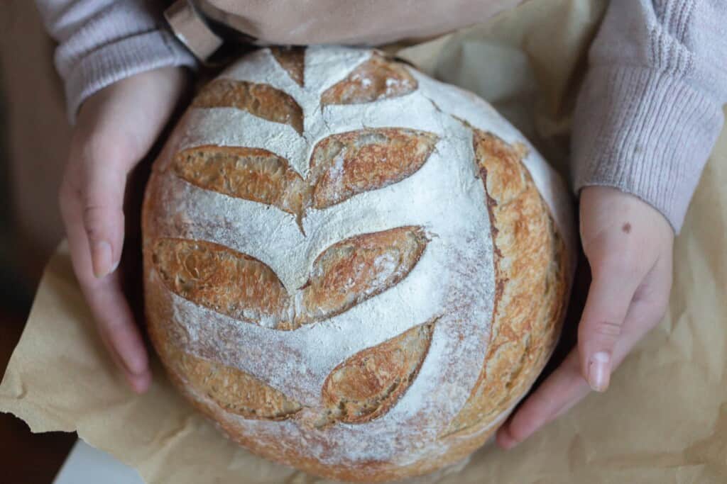 Honey sourdough loaf held in a woman's hands with parchment paper underneath