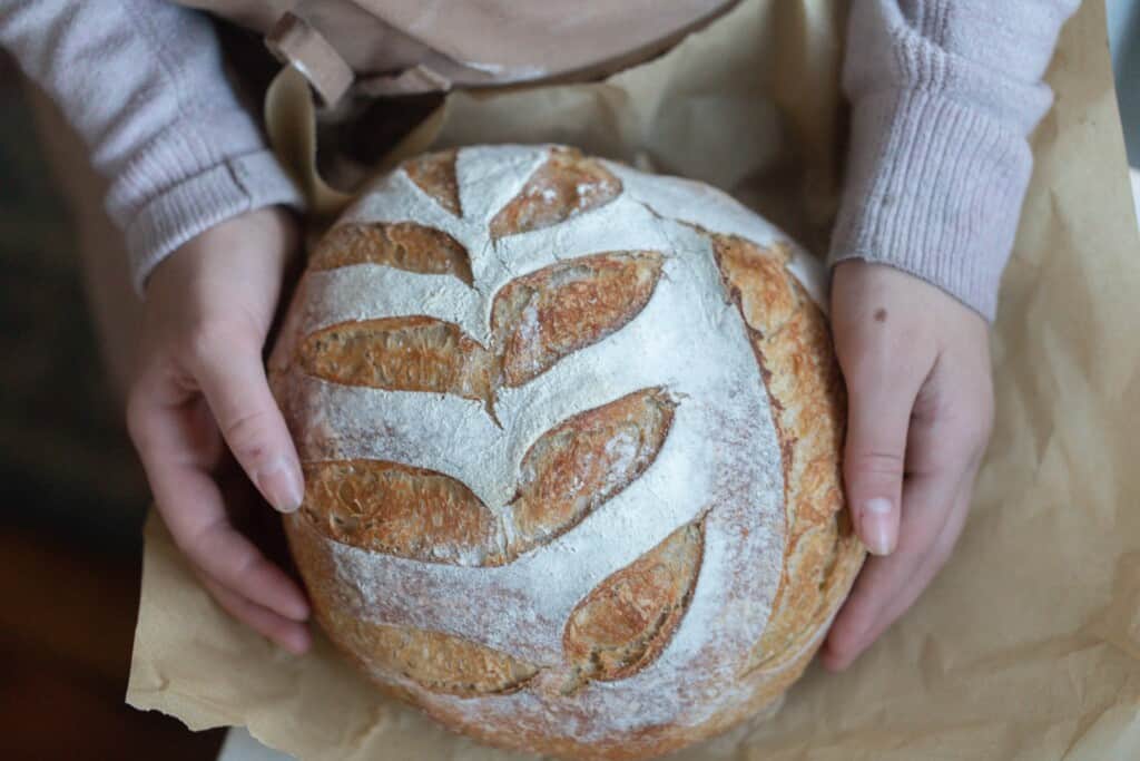 hands holding a loaf of honey sourdough bread on parchment paper