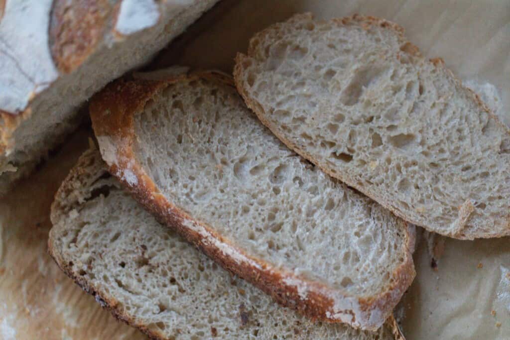 Three slices of honey sourdough bread next to a full boule