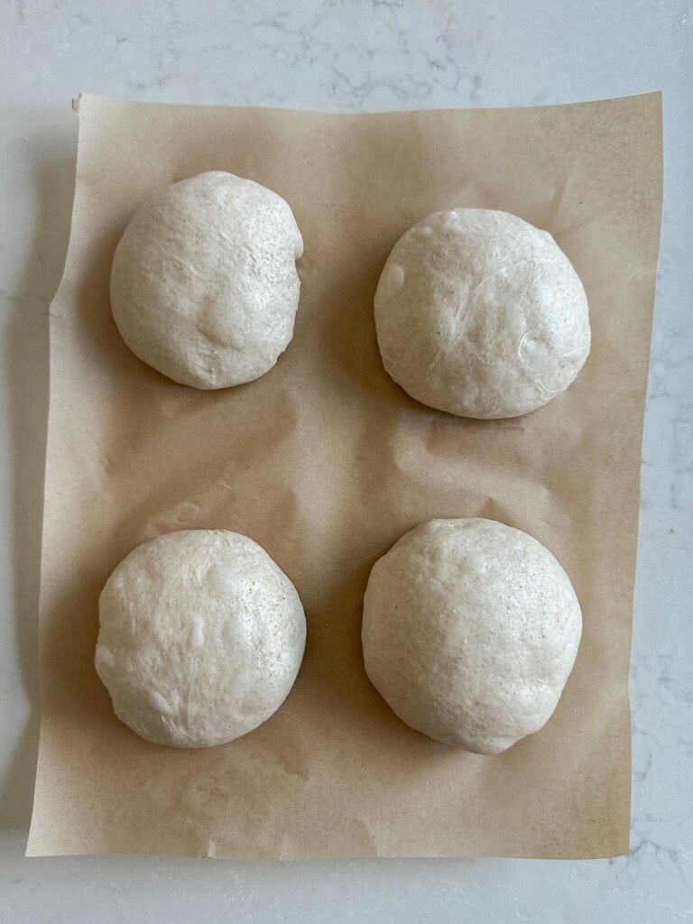 Four dough balls on parchment paper on a white countertop