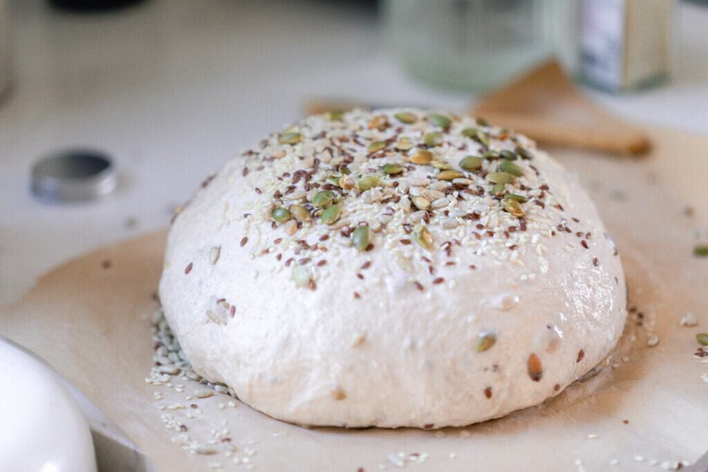 Loaf of seeded sourdough bread on parchment paper ready for the oven