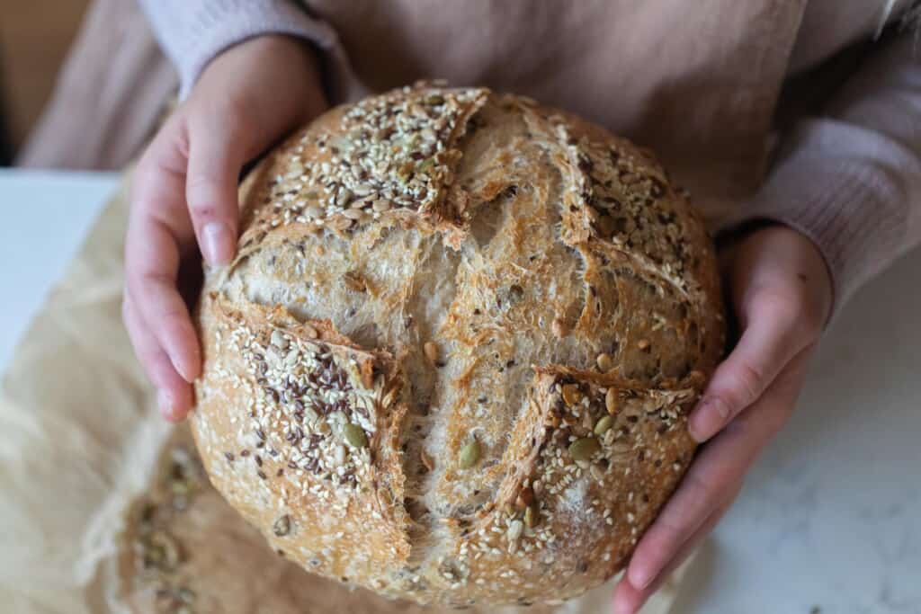 Two hands holding a loaf of seeded sourdough bread