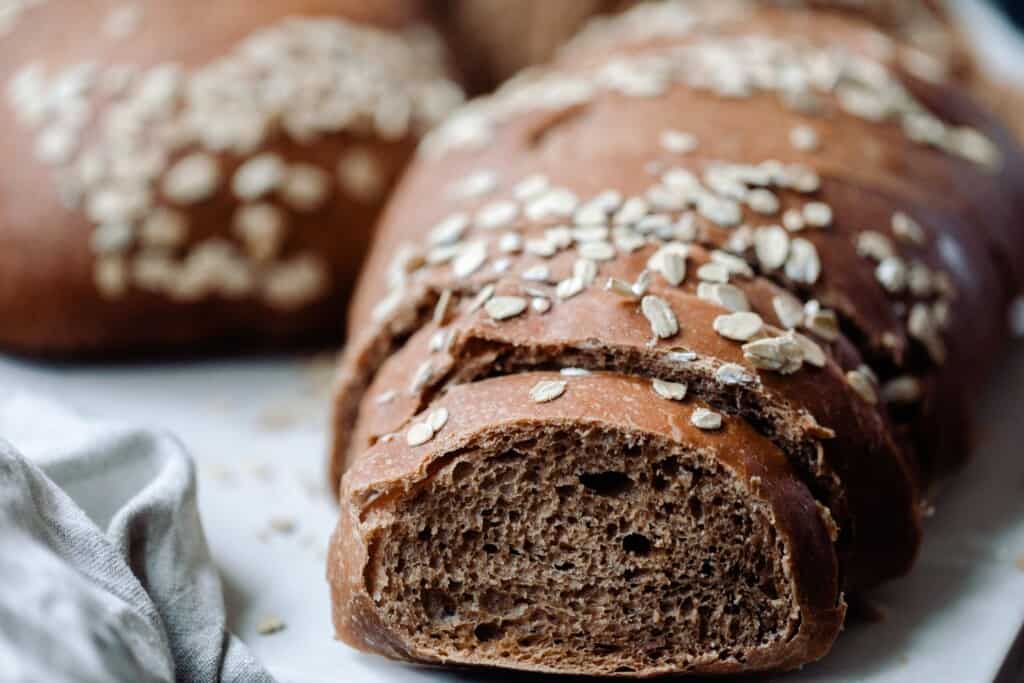 Loaf of brown bread cut into with another loaf in background on a white countertop