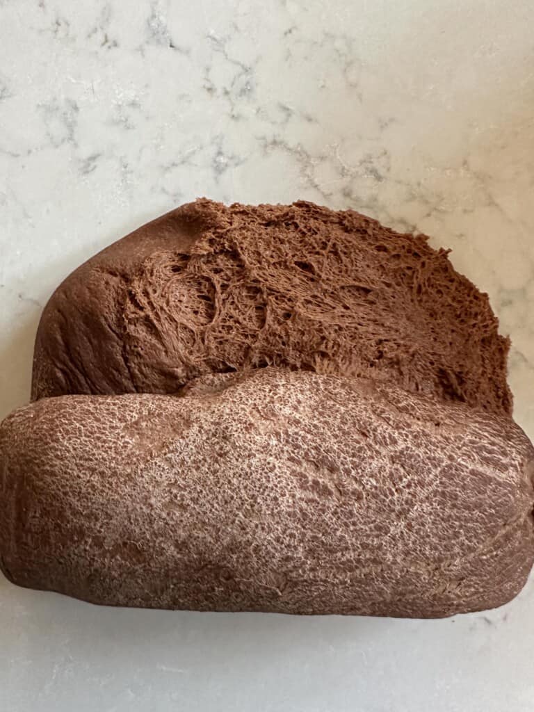 rolling up bread dough on a floured white countertop