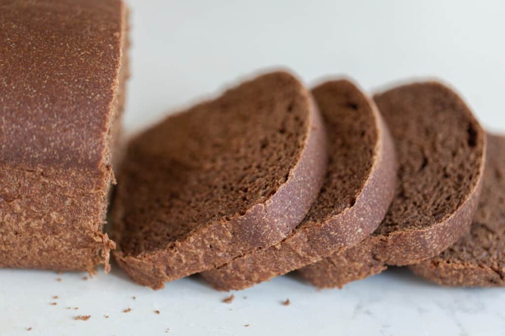 a loaf of sourdough pumpernickel bread with four slices laying on a white countertop