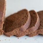 a loaf of sourdough pumpernickel bread with four slices laying on a white countertop