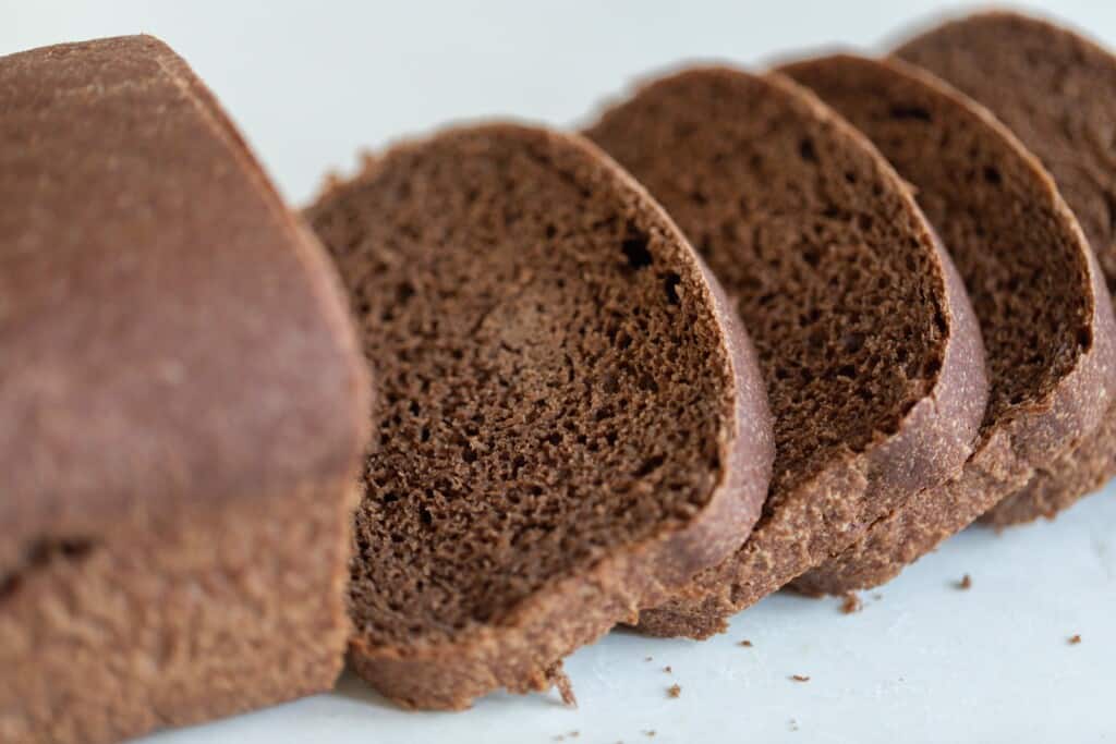 a loaf of sourdough pumpernickel bead with four slices resting on the white countertop