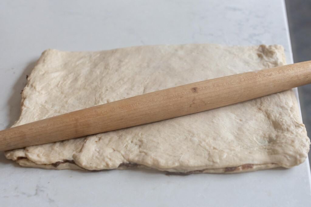 dough folded over in a rectangle in a white countertop with a rolling pin on top