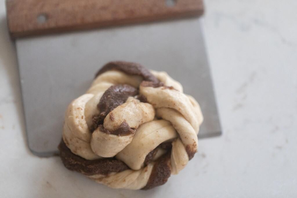 Swedish buns on a white countertop with a bench scraper under half of the bun