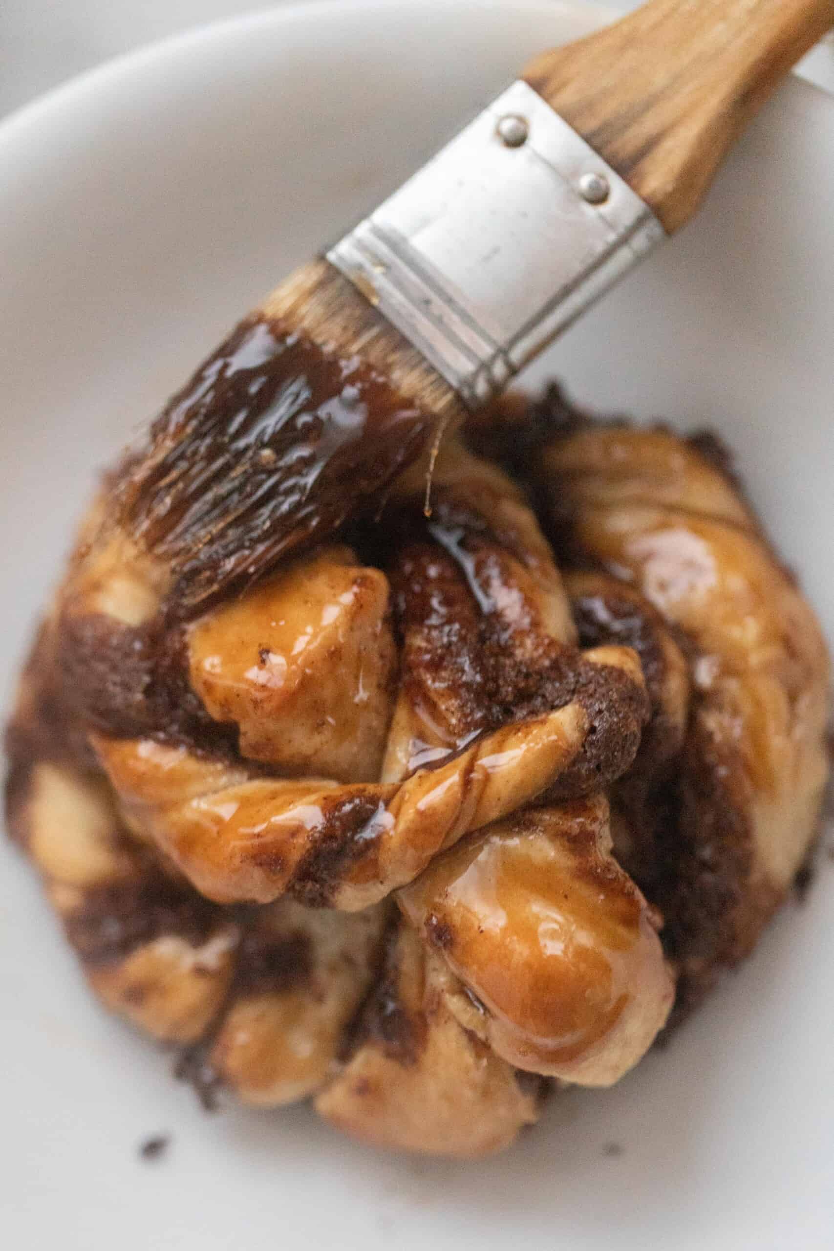 A Swedish cinnamon bun on a white countertop being brushed with a brown sugar glaze