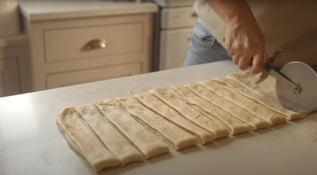 women cutting dough with cinnamon filling into strips with a pizza cutter