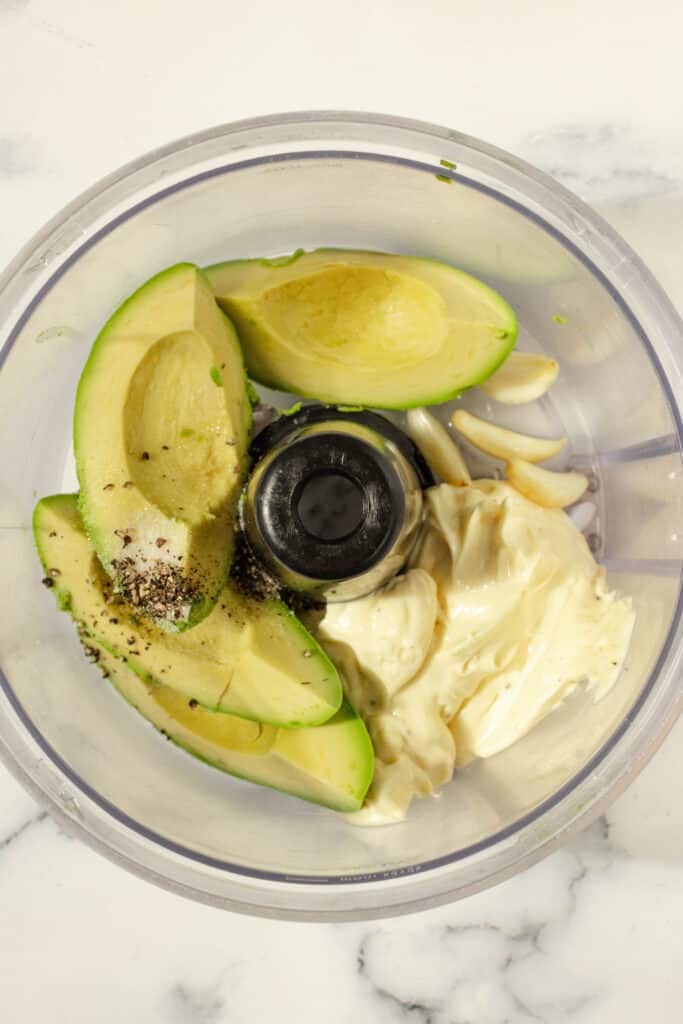 Avocado aioli ingredients in a food processor on a white countertop