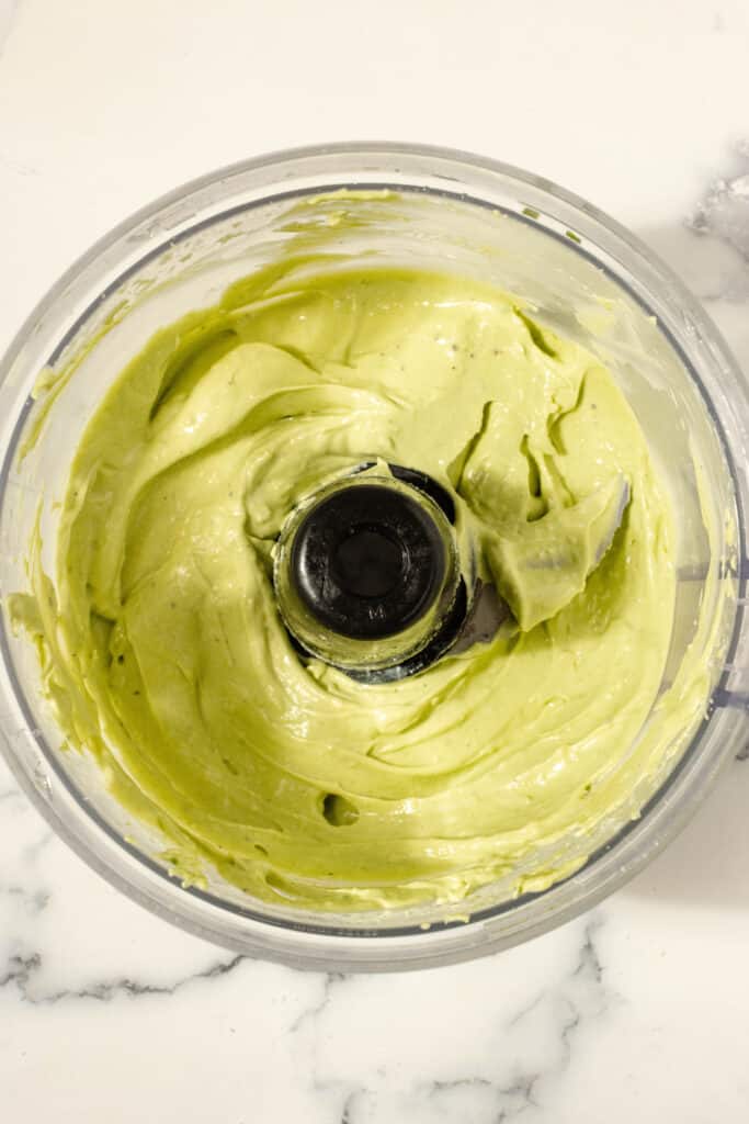 Avocado aioli mixed together in a food processor on a white countertop