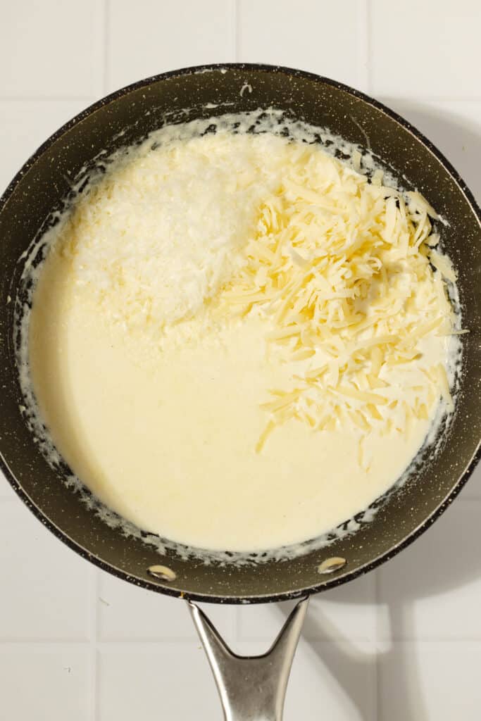 two kinds of cheese added to a creamy sauce in a skillet