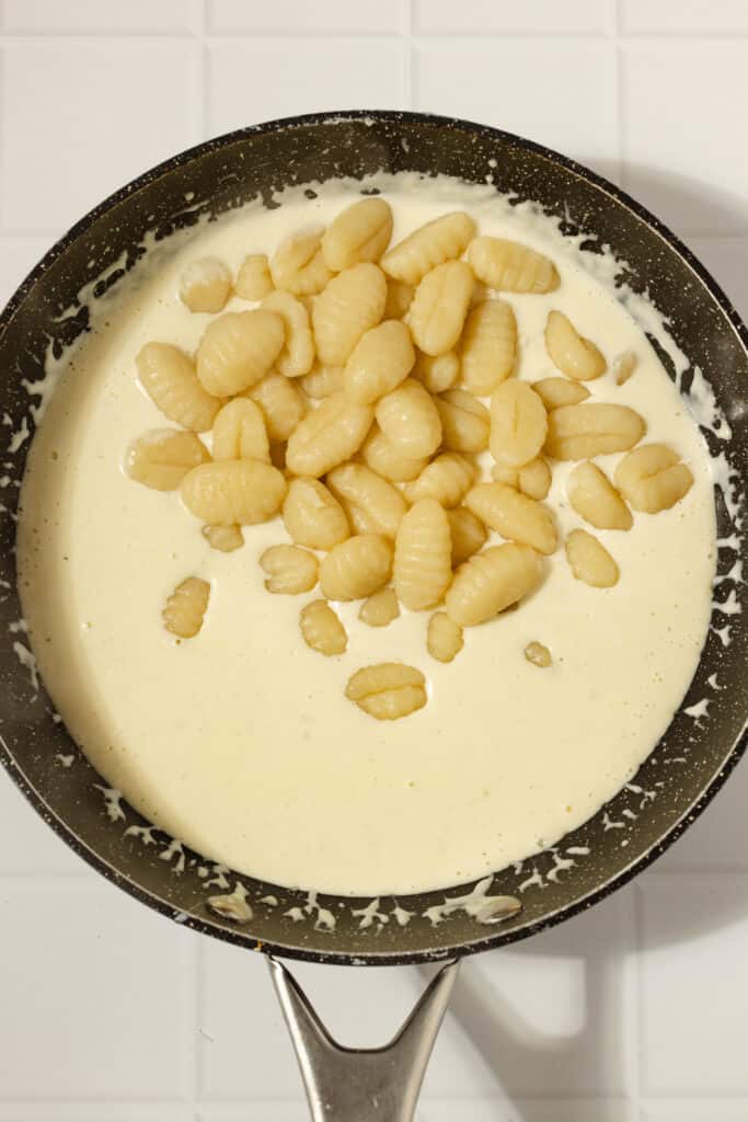 cooked gnocchi added to a creamy sauce in a skillet