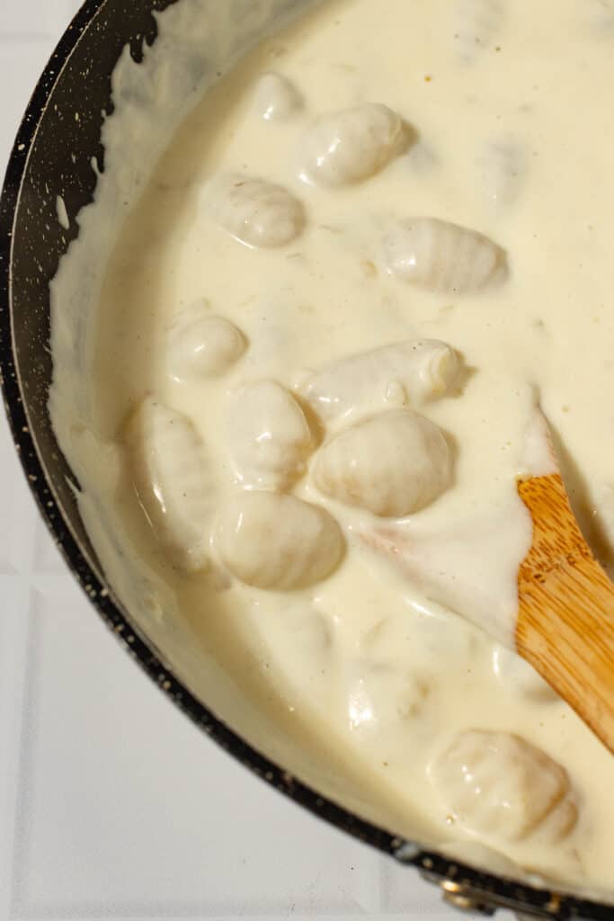 gnocchi being stirred into a cream sauce with a wooden spoon in a skillet