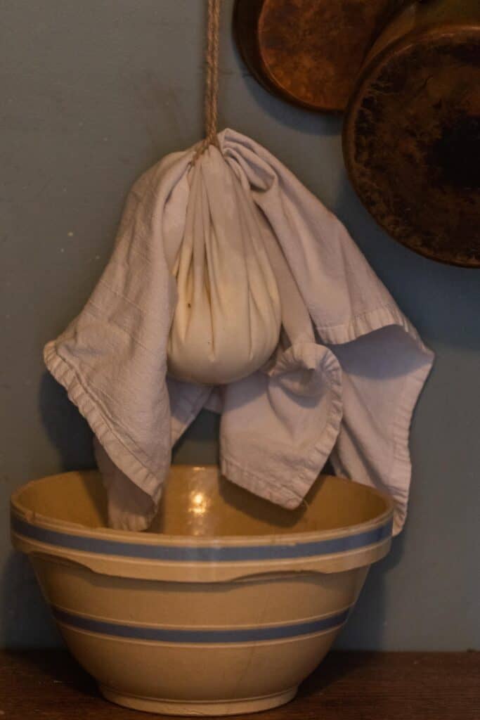 kefir cheese draining into a bowl while hanging wrapped in a flour sack towel