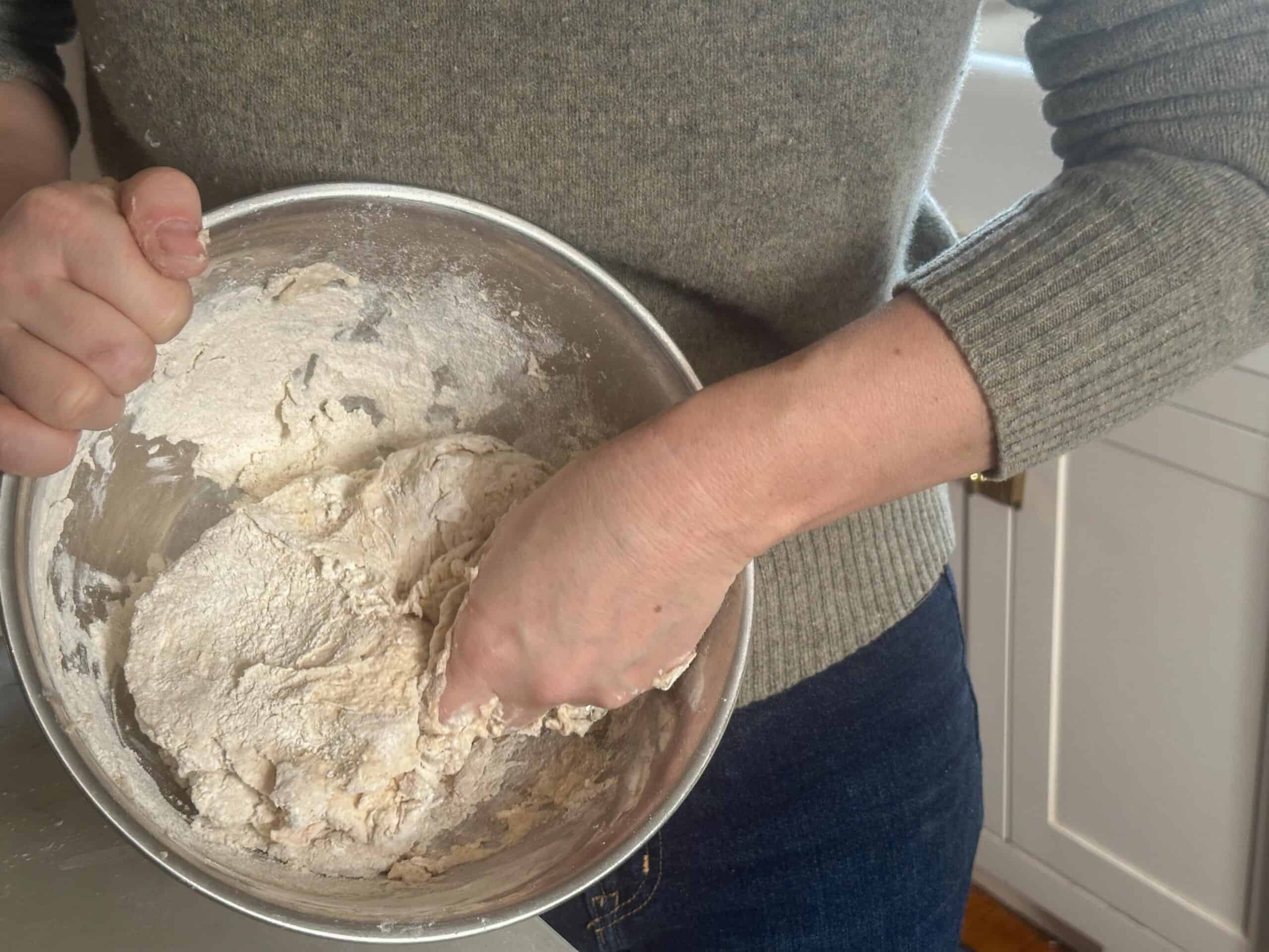 woman mixing sourdough dough by hand in a silver bowl