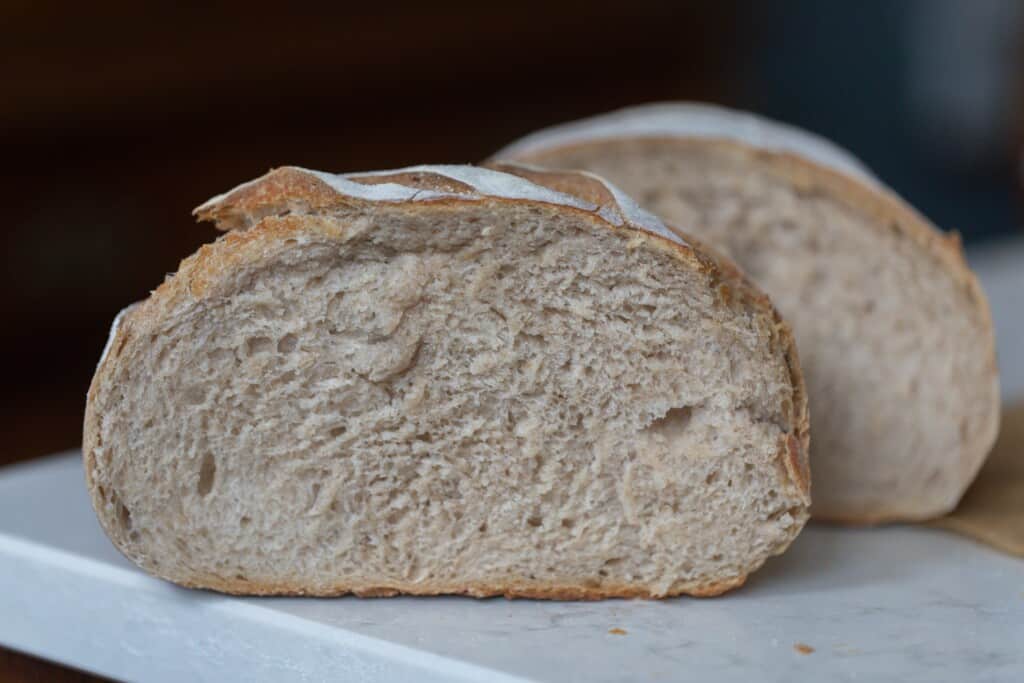 Two halves of a low hydration sourdough bread on a white countertop