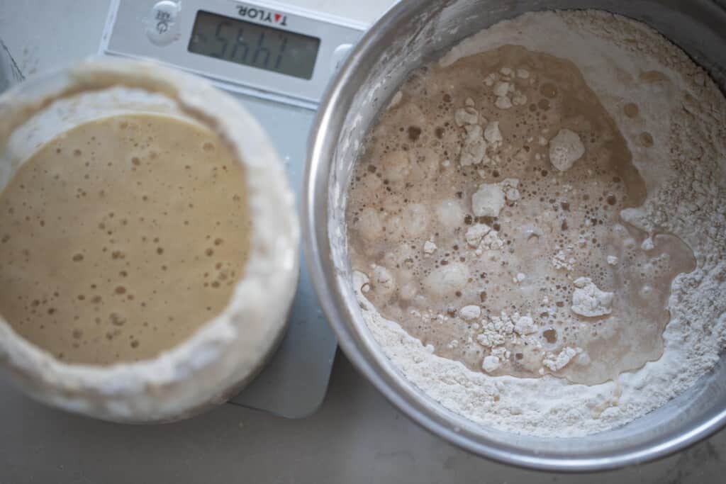A large bowl with ingredients next to a kitchen scale with a sourdough starter being measured