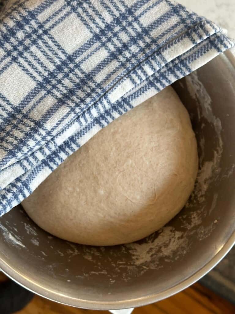 Low hydration sourdough dough ball in a large bowl covered with a blue and white checkered tea towel